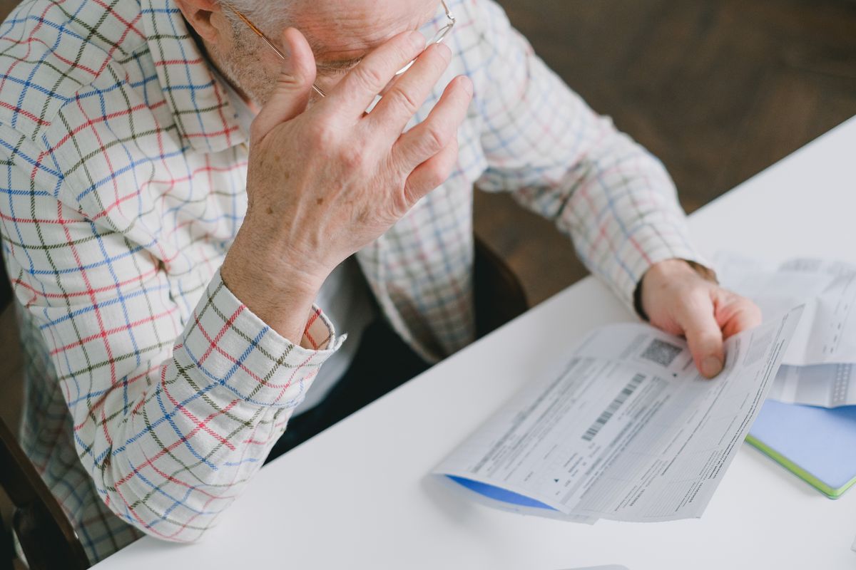An older man reading a printed statement at his kitchen table.